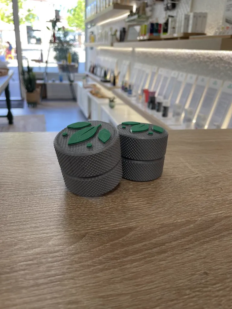 Petites boîtes grises moletées au couvercle orné d’un logo vert, posées sur le comptoir en bois d’une boutique
