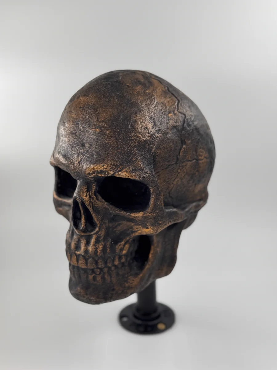 Crâne décoratif imprimé en 3D, finition bronze vieilli, posé sur un socle noir