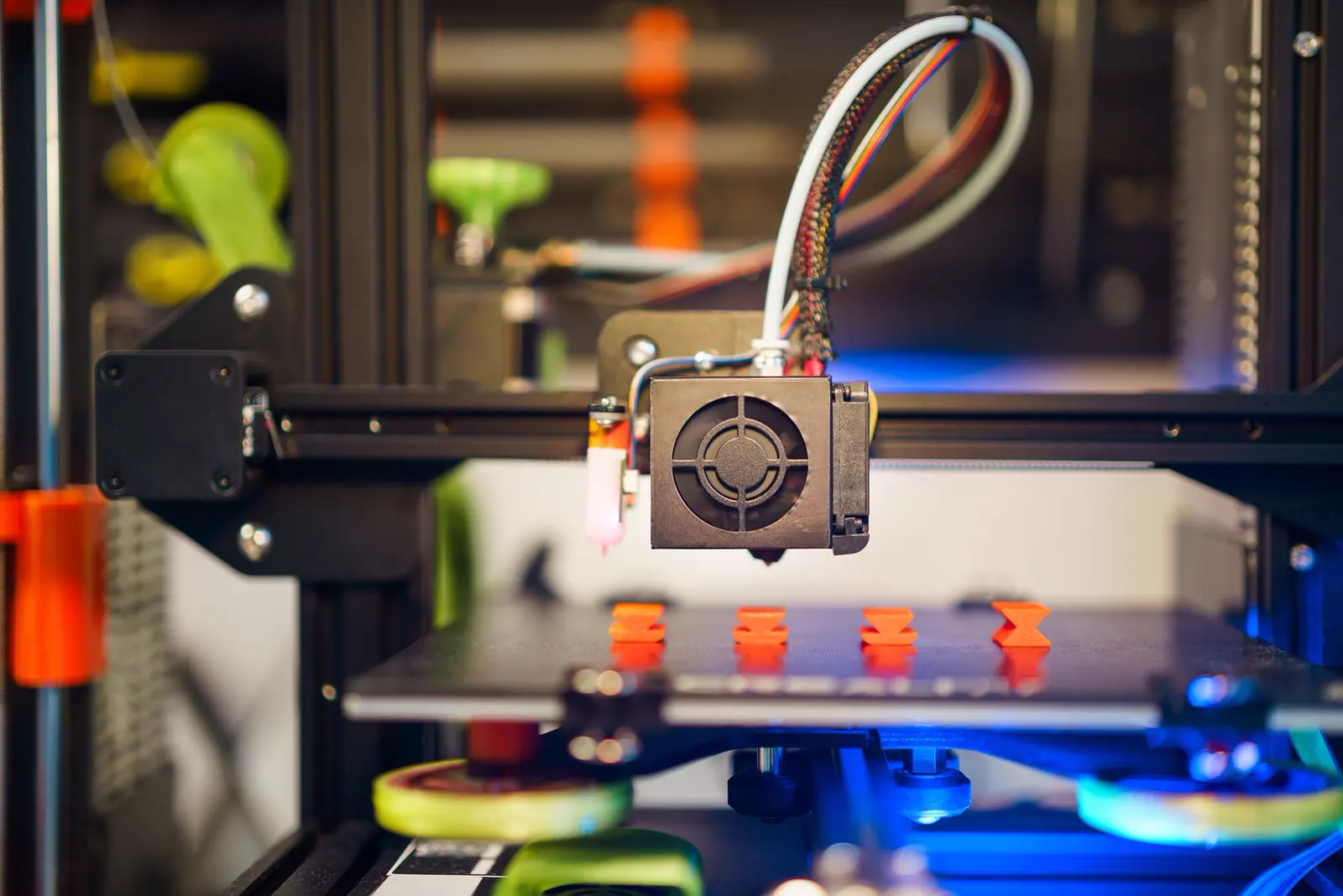 Imprimante 3D à filament vue de face, avec quatre petites pièces orange alignées sur son plateau