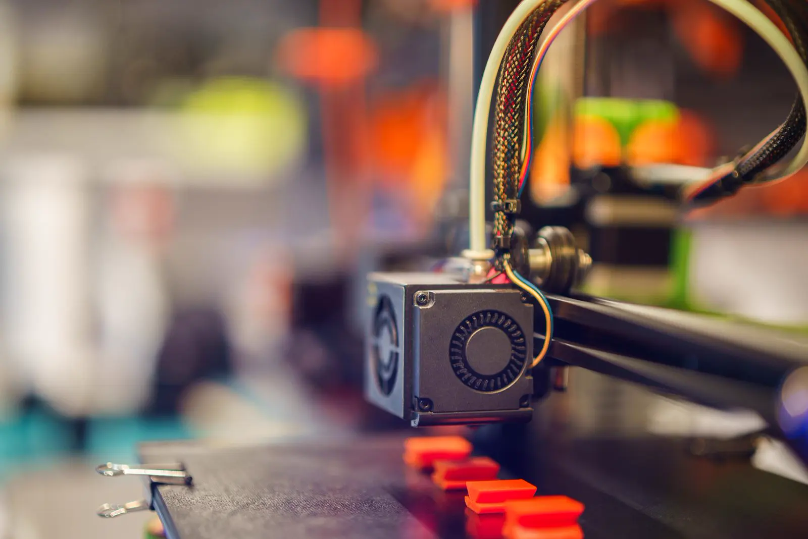 Tête d’impression d’une imprimante 3D au-dessus d’un plateau portant de petites pièces orange